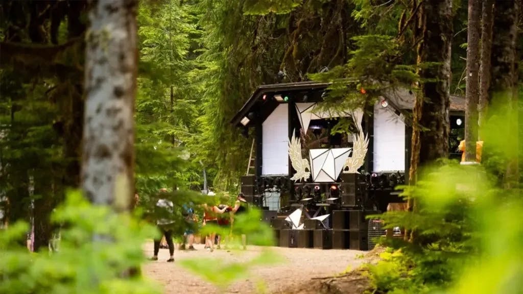 A glimpse of the Asgard stage through the forest, with people dancing in the daylight.