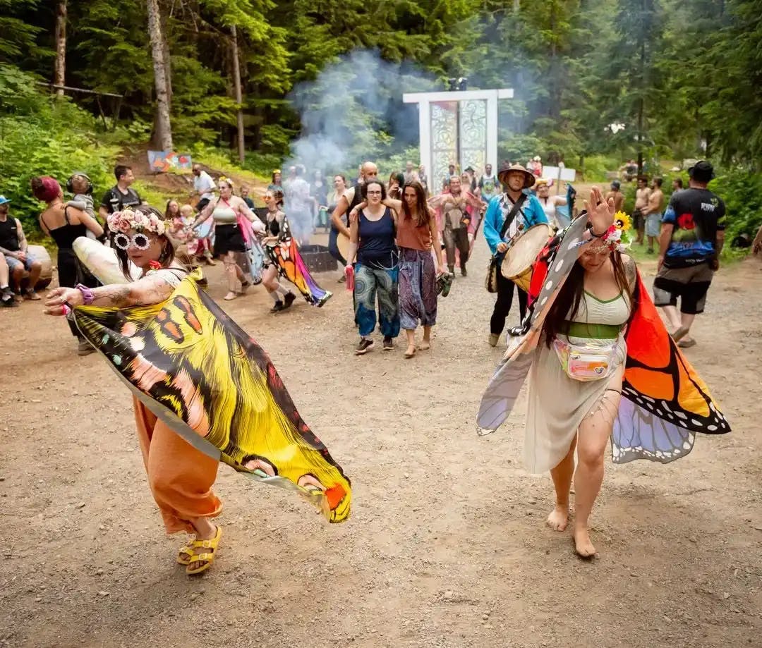 A colorful ValhallaFest parage in a forest with costumed participants and a smoky entrance arch.