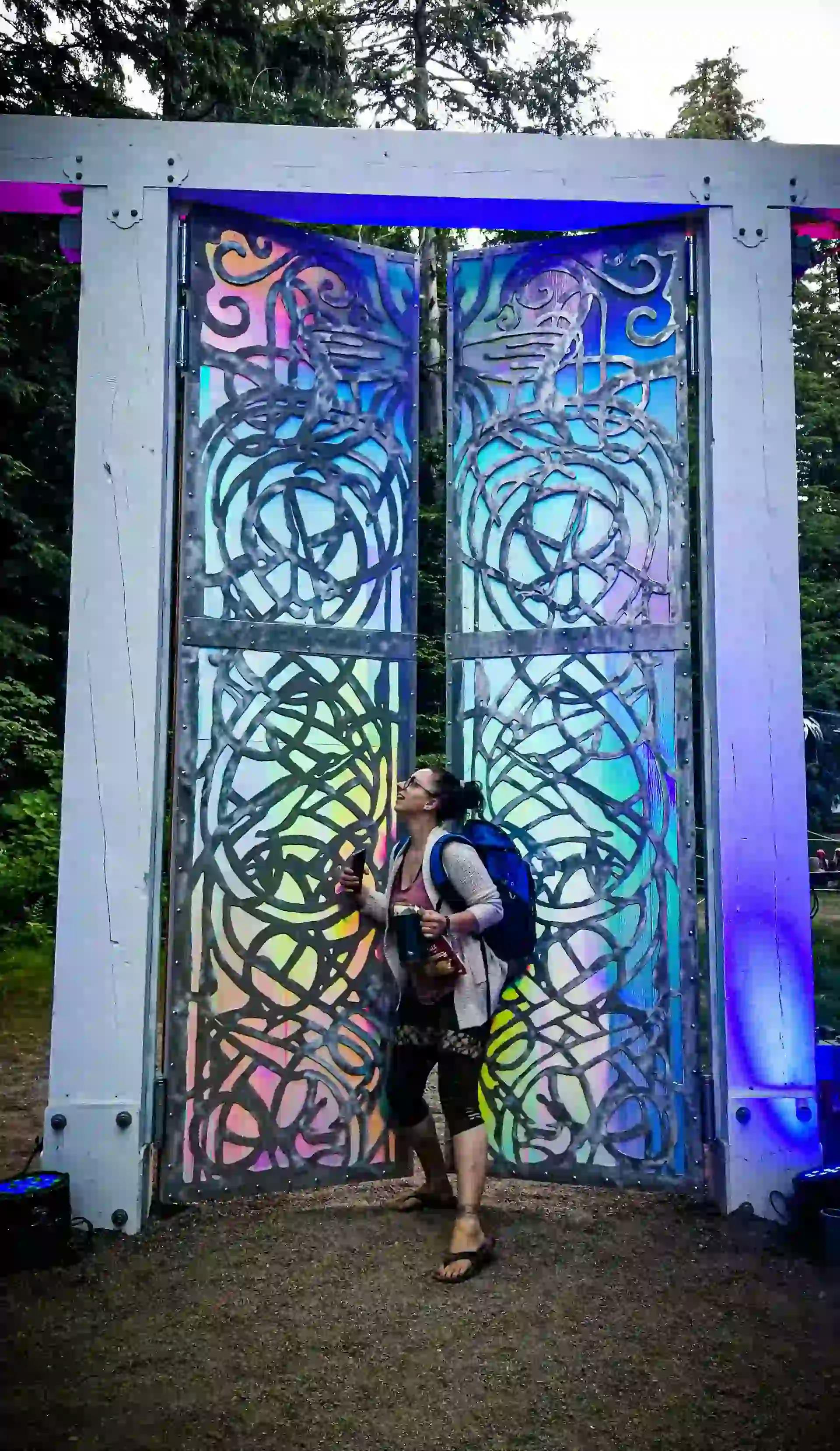 A festival attendee standing before a tall, ornate gate with kaleidoscopic panels.