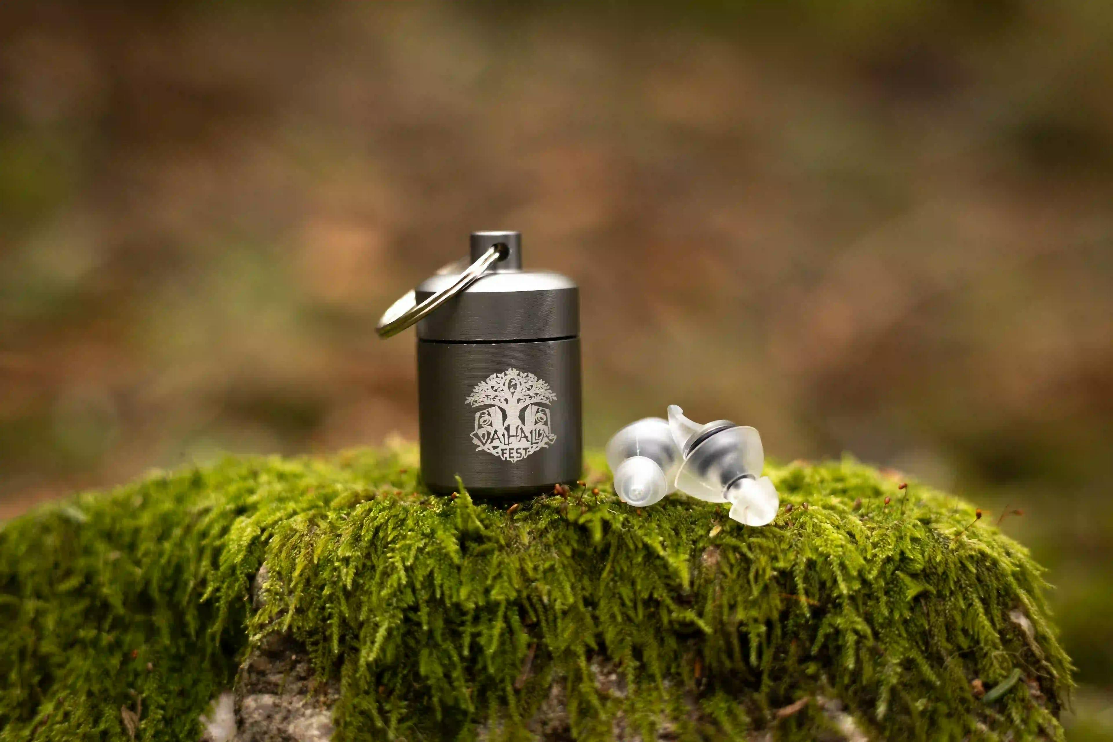 ValhallaFest branded earplugs in case displayed on a mossy stone.