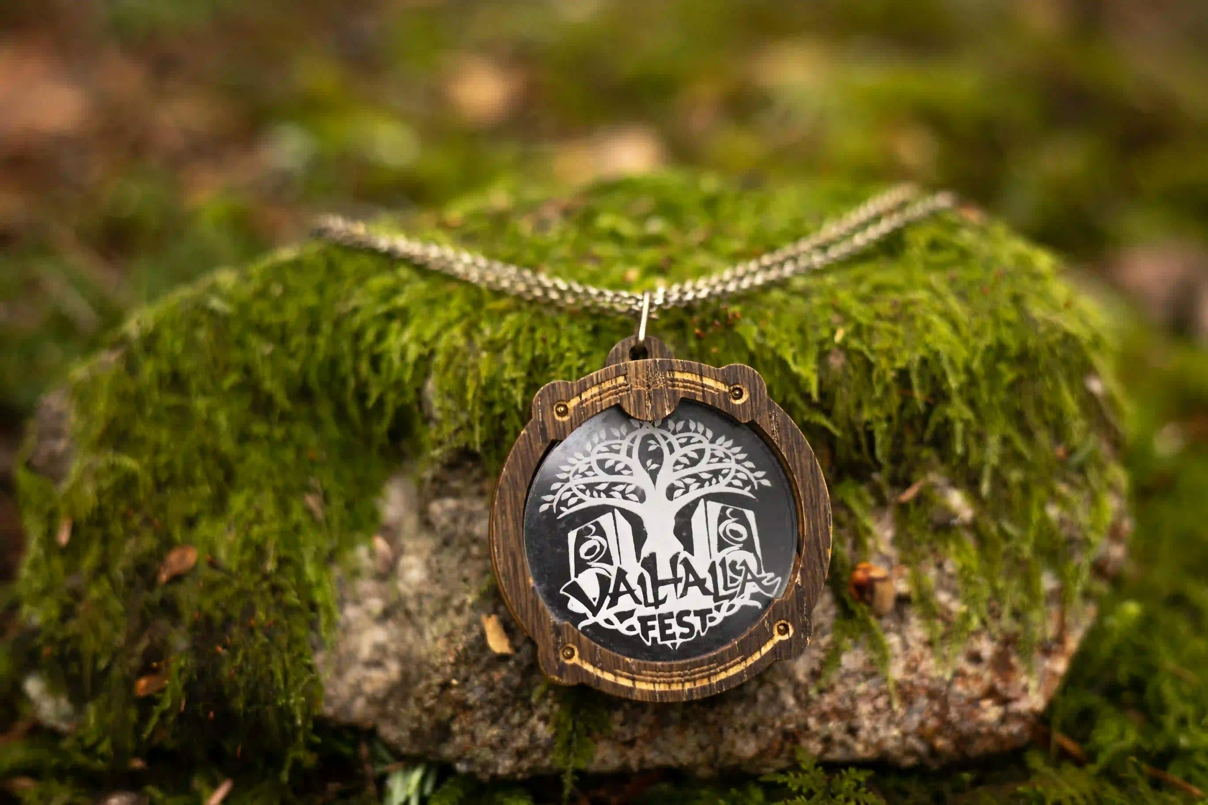 Wooden ValhallaFest pendant necklace displayed on a mossy stone.