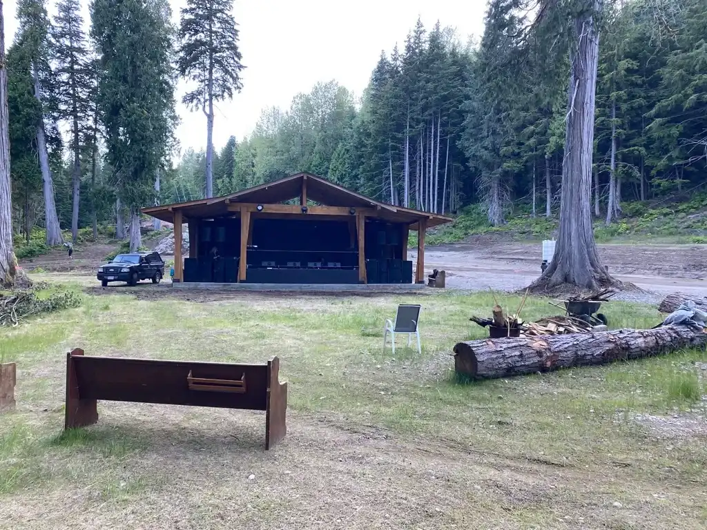 The AgeHa stage at dusk, with seating logs and a fire pit in the foreground.