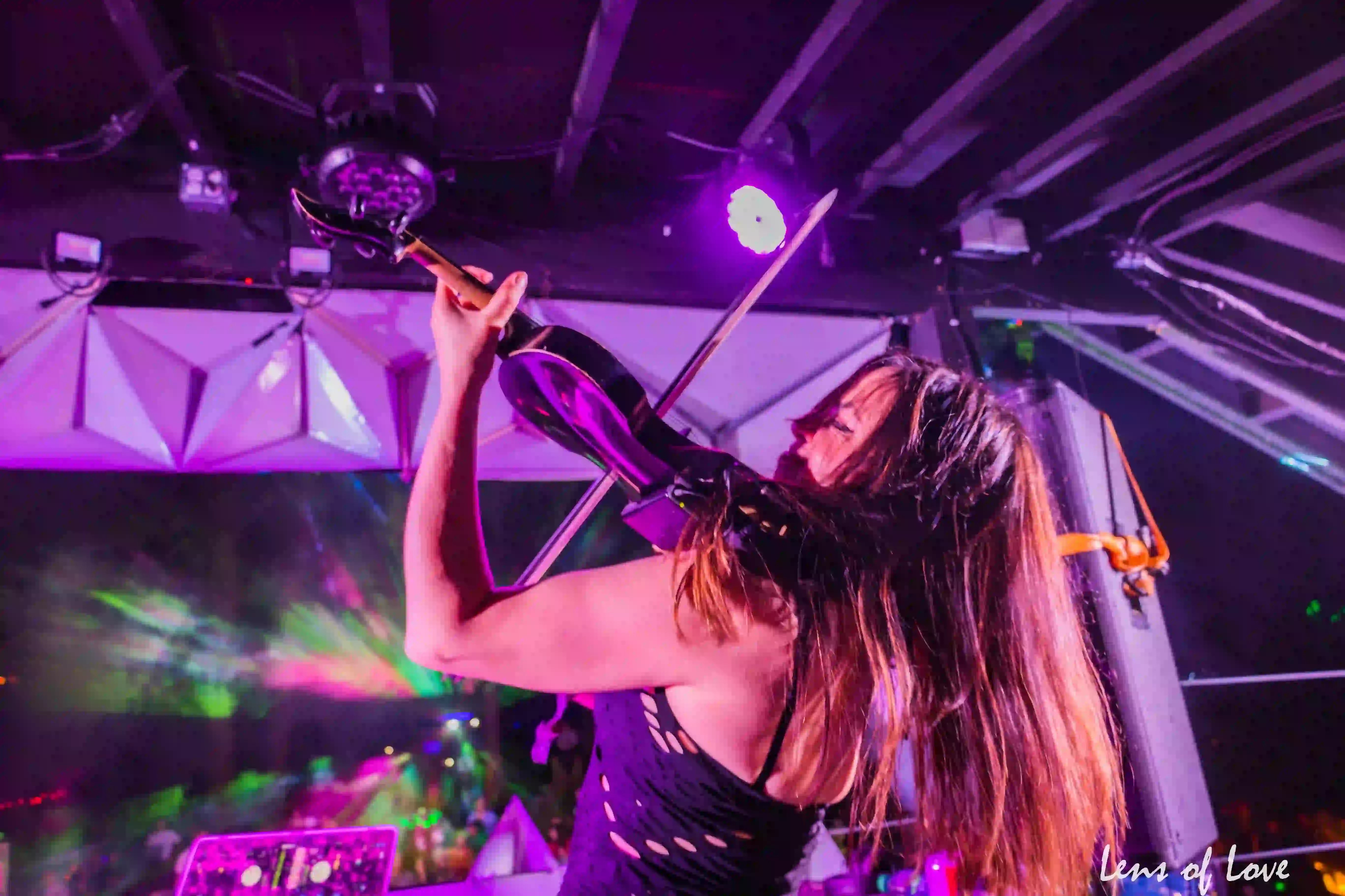 Violinist energetically performing on the Asgard stage with vibrant lighting in the background.