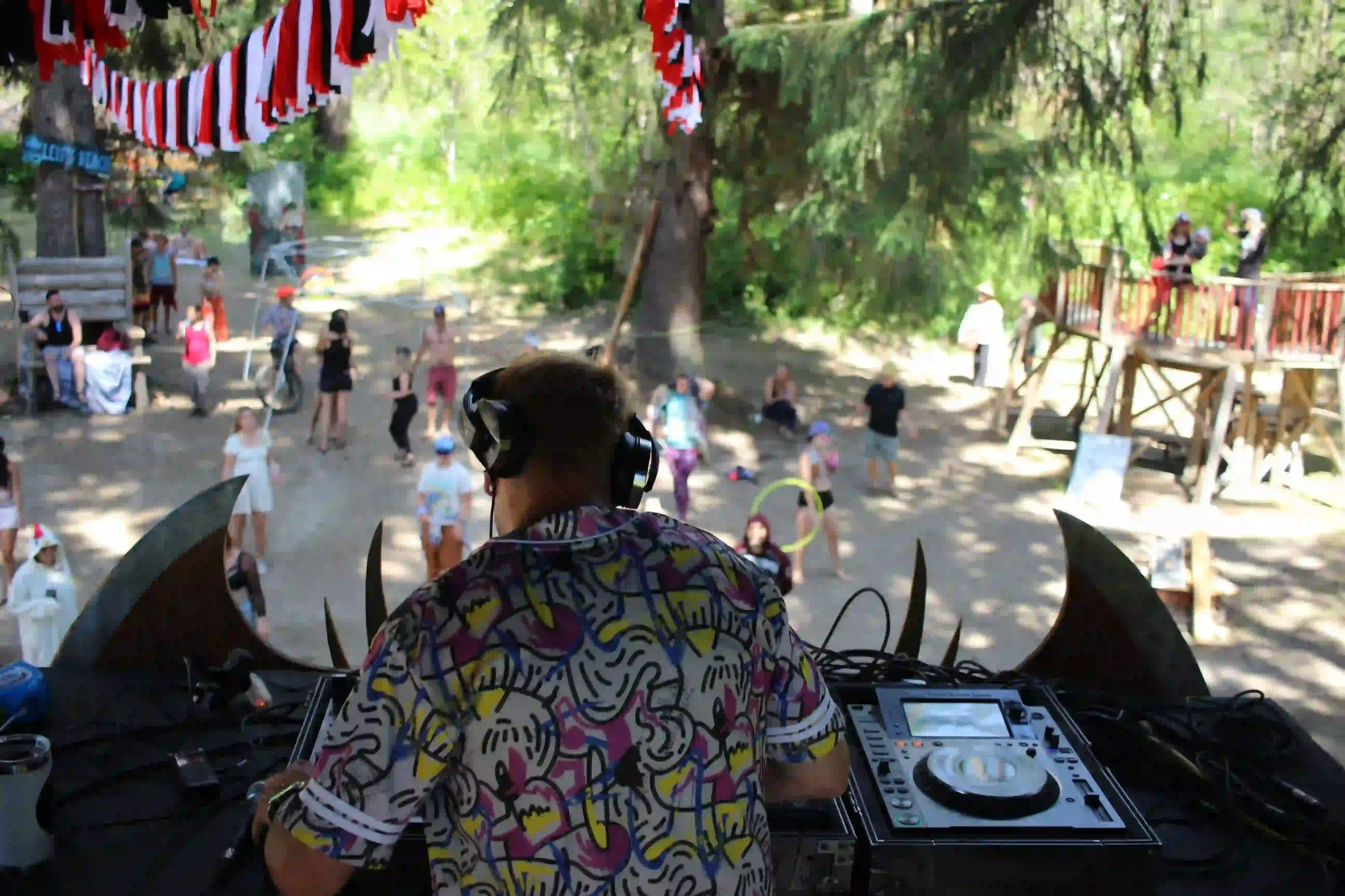 Leif's Beach stage at ValhallaFest with a casual atmosphere, market stalls, and forest backdrop.