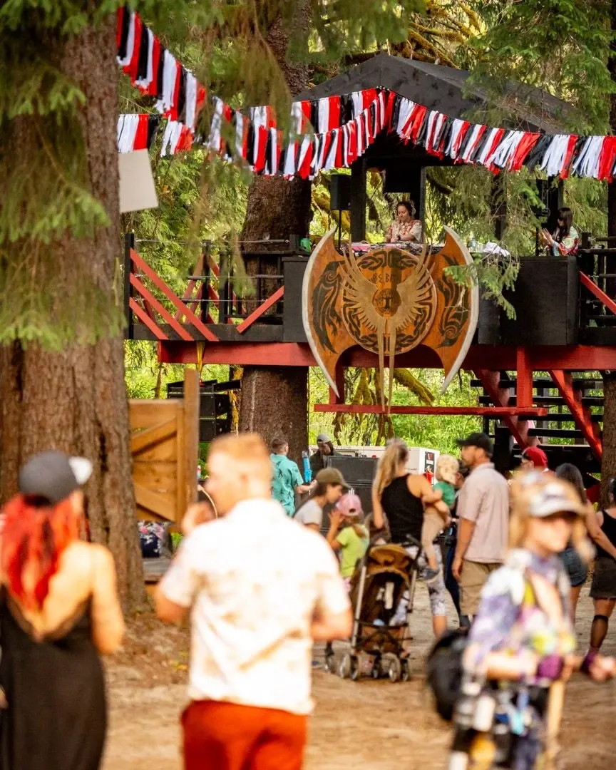 Leif's Beach stage at ValhallaFest with a casual atmosphere, market stalls, and forest backdrop.