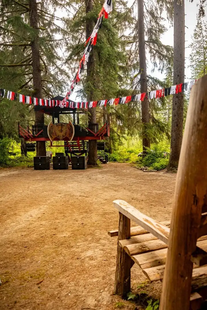 Leif's Beach stage at ValhallaFest with a casual atmosphere, market stalls, and forest backdrop.