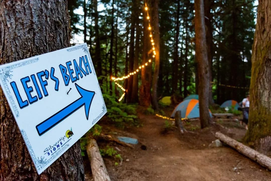 Leif's Beach stage at ValhallaFest with a casual atmosphere, market stalls, and forest backdrop.