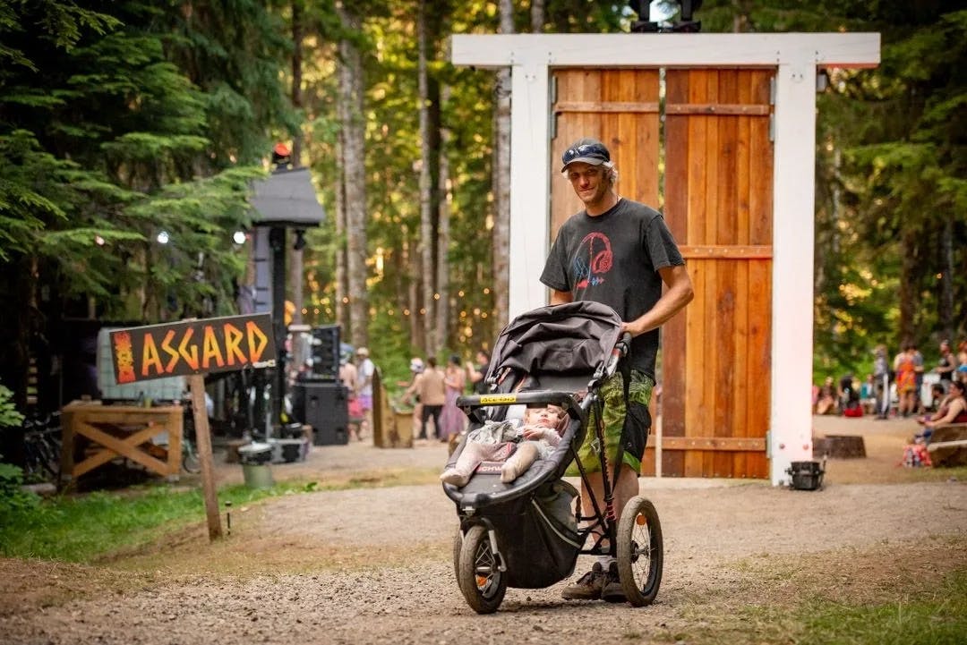 A man pushing a stroller through a festival site with 'Asgard' sign in the background.