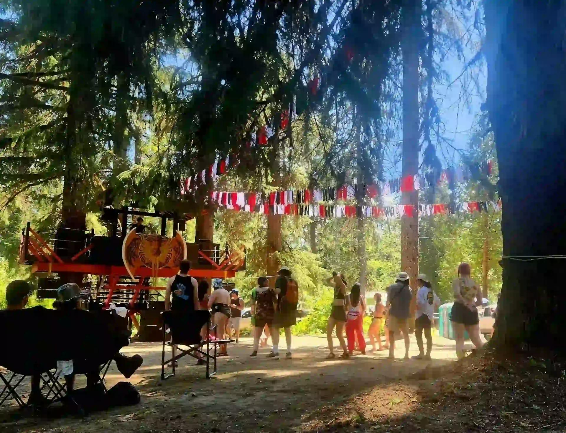 Leif's Beach stage at ValhallaFest with a casual atmosphere, market stalls, and forest backdrop.